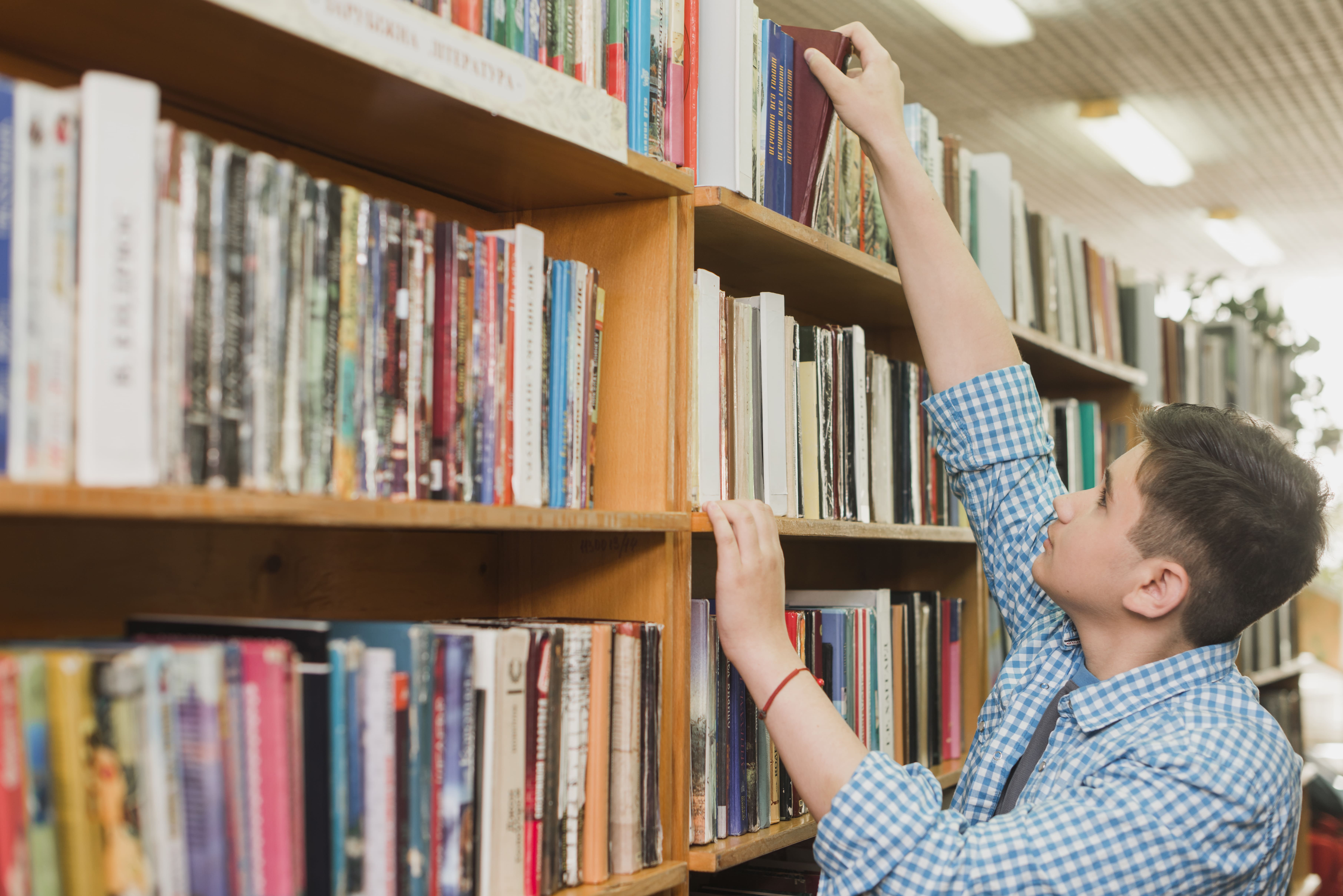 male teenager picking book from bookshelf